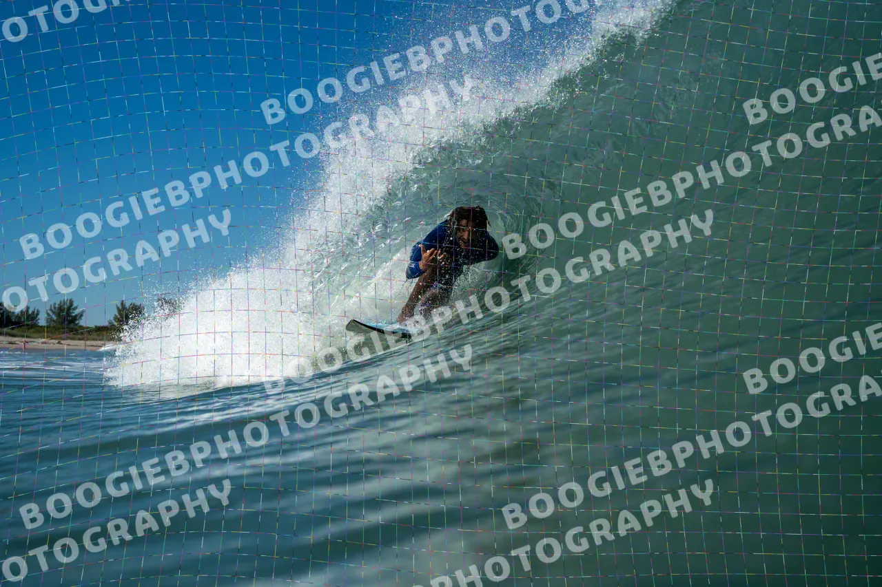 Surfer crouched inside a clean blue-green barrel, spray fanning off the lip, a low treeline on the horizon.