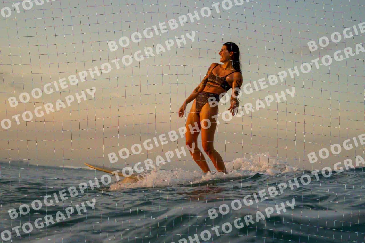 Longboarder standing tall on a pale board at sunset, stepping toward the nose, pastel sky behind.