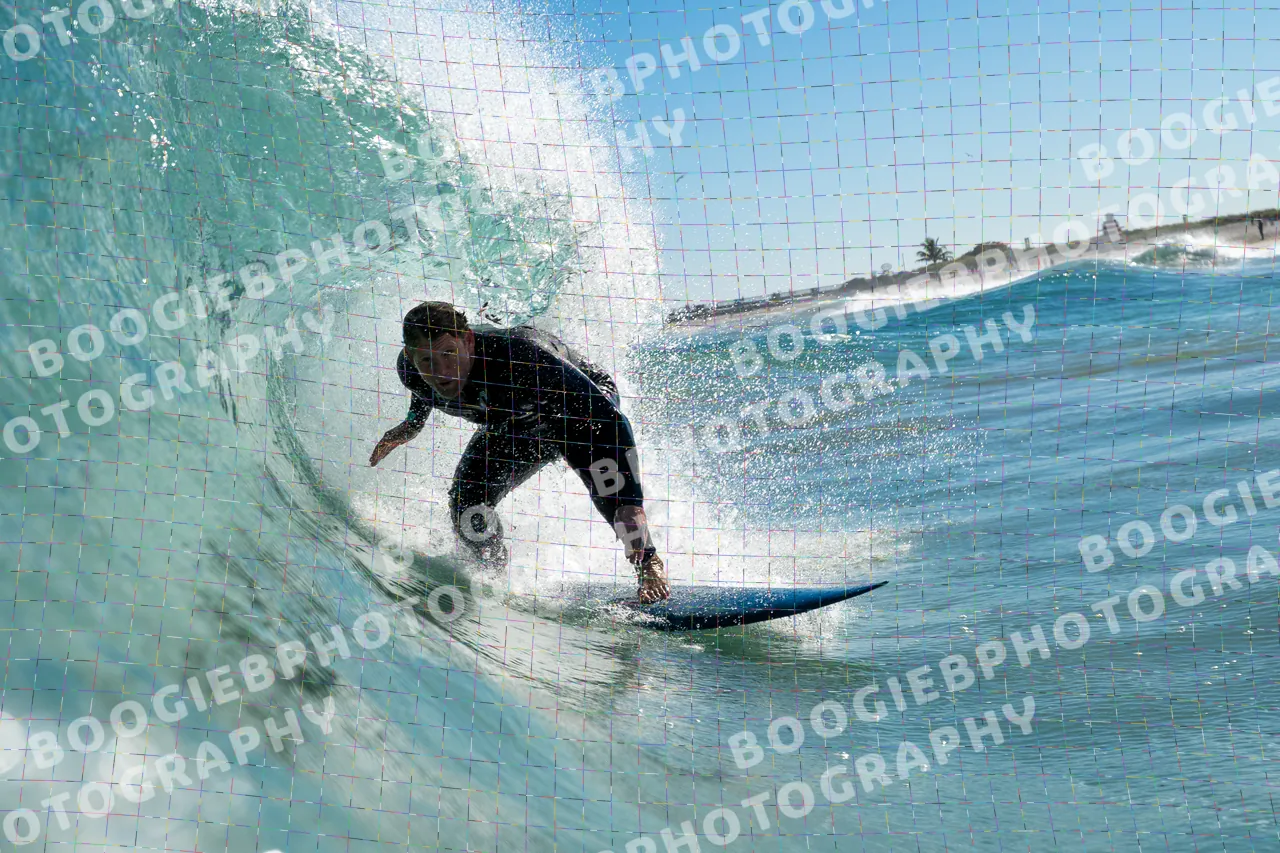 Surfer in a black wetsuit driving out of a hollow section, hand dragging in the face, beach and palms behind.