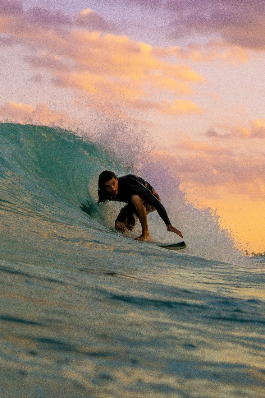 Surfer tucked into a barrel under a purple and orange sunset sky.
