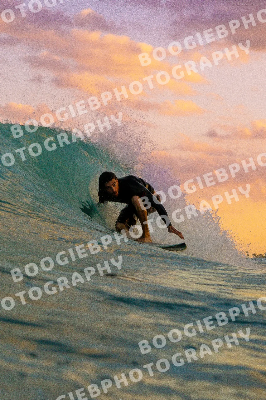 Surfer tucked into a barrel under a purple and orange sunset sky.
