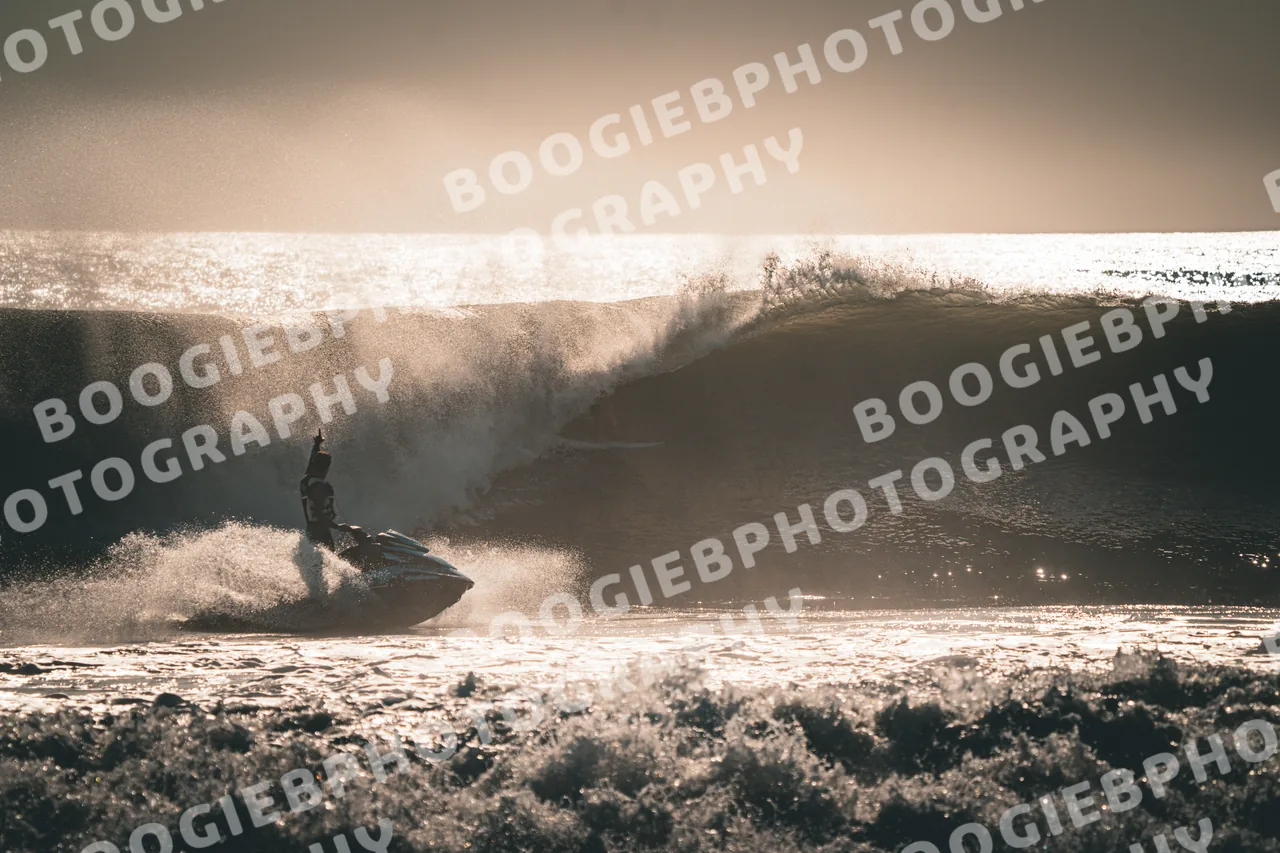 Jet ski throwing a wall of spray in front of a backlit wave, the whole frame washed gold.