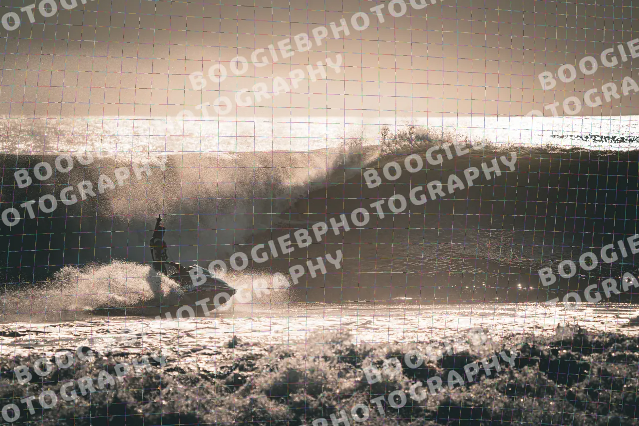 Jet ski throwing a wall of spray in front of a backlit wave, the whole frame washed gold.