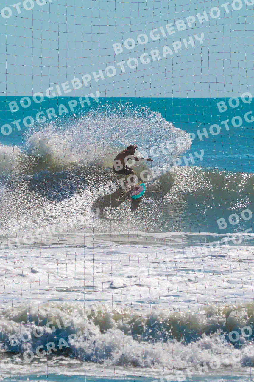 Surfer snapping off the top of a small teal wave, shot from the beach across lines of whitewater.