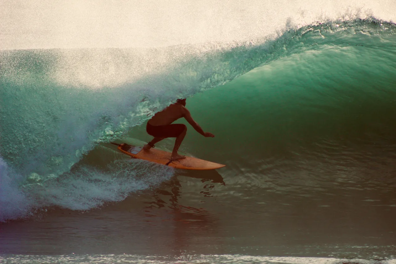 Surfer riding a green barrel at golden hour on an orange board, backlit spray blowing off the crest.