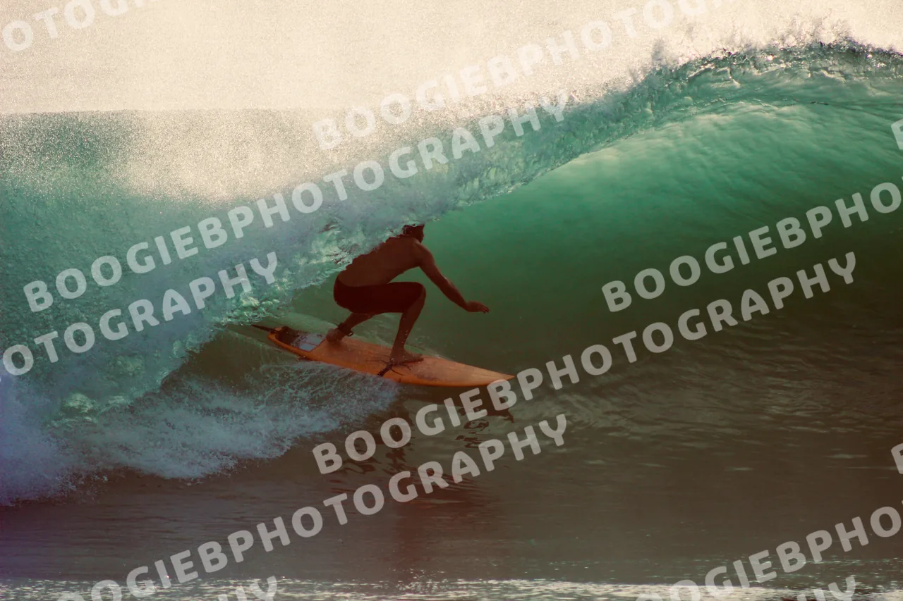 Surfer riding a green barrel at golden hour on an orange board, backlit spray blowing off the crest.